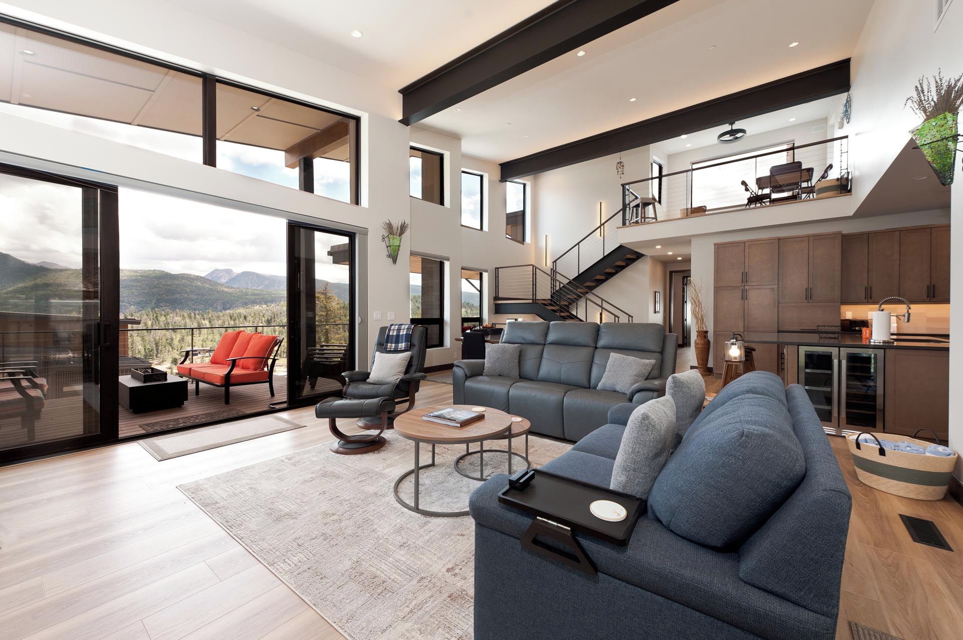 A spacious living area with a large sofa, a coffee table, and a balcony with a view of the mountains.