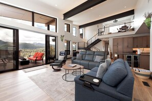 A spacious living area with a large sofa, a coffee table, and a balcony with a view of the mountains. - Brand new home at Purgatory Resort - Hot Tub/Sauna/3 Decks/AC/Amazing Views (Durango)