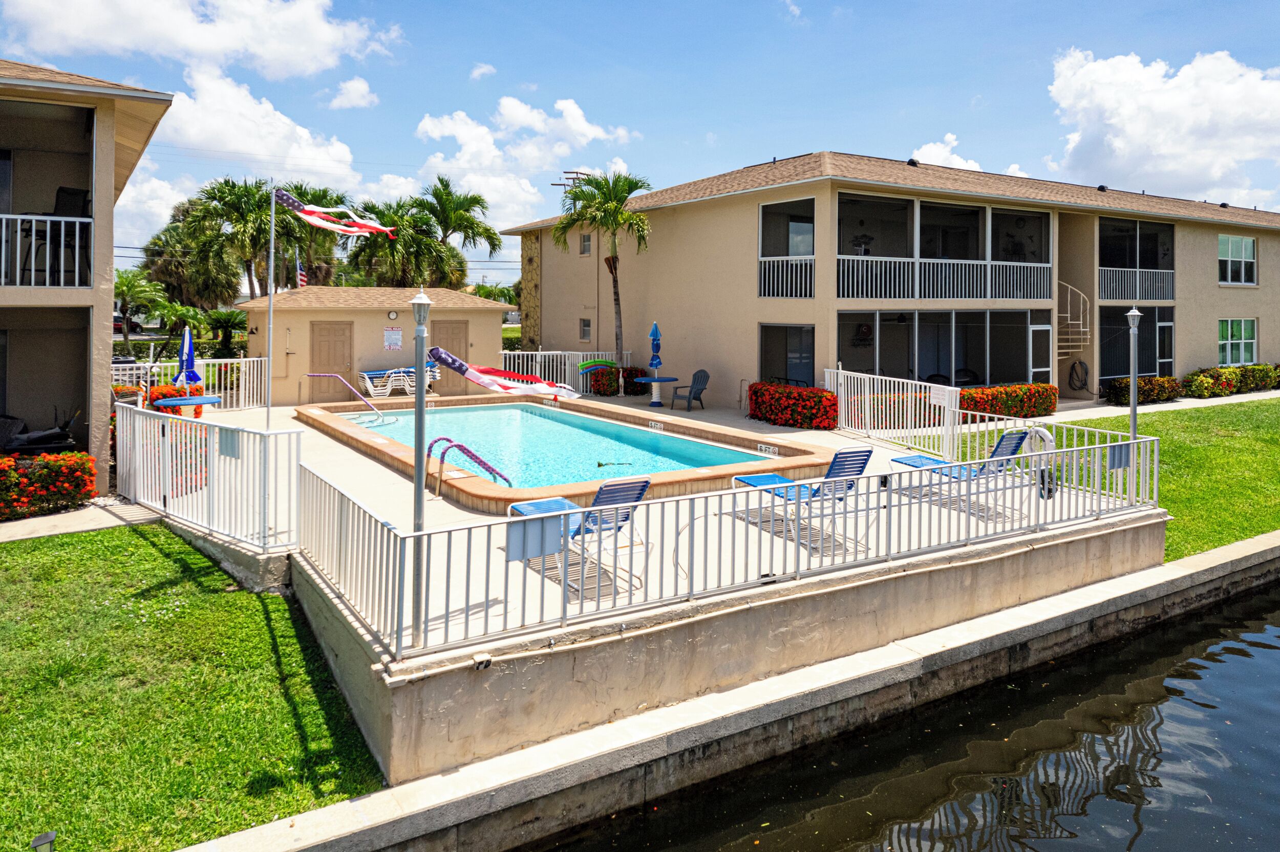 A swimming pool with a white fence, lounge chairs, and a flag.