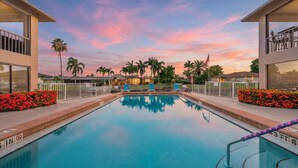 Piscina com vista para o pôr do sol, cercada por palmeiras e uma grade.