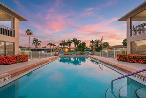 Ein Swimmingpool mit Sonnenuntergangsblick, umgeben von Palmen und einem Zaun.