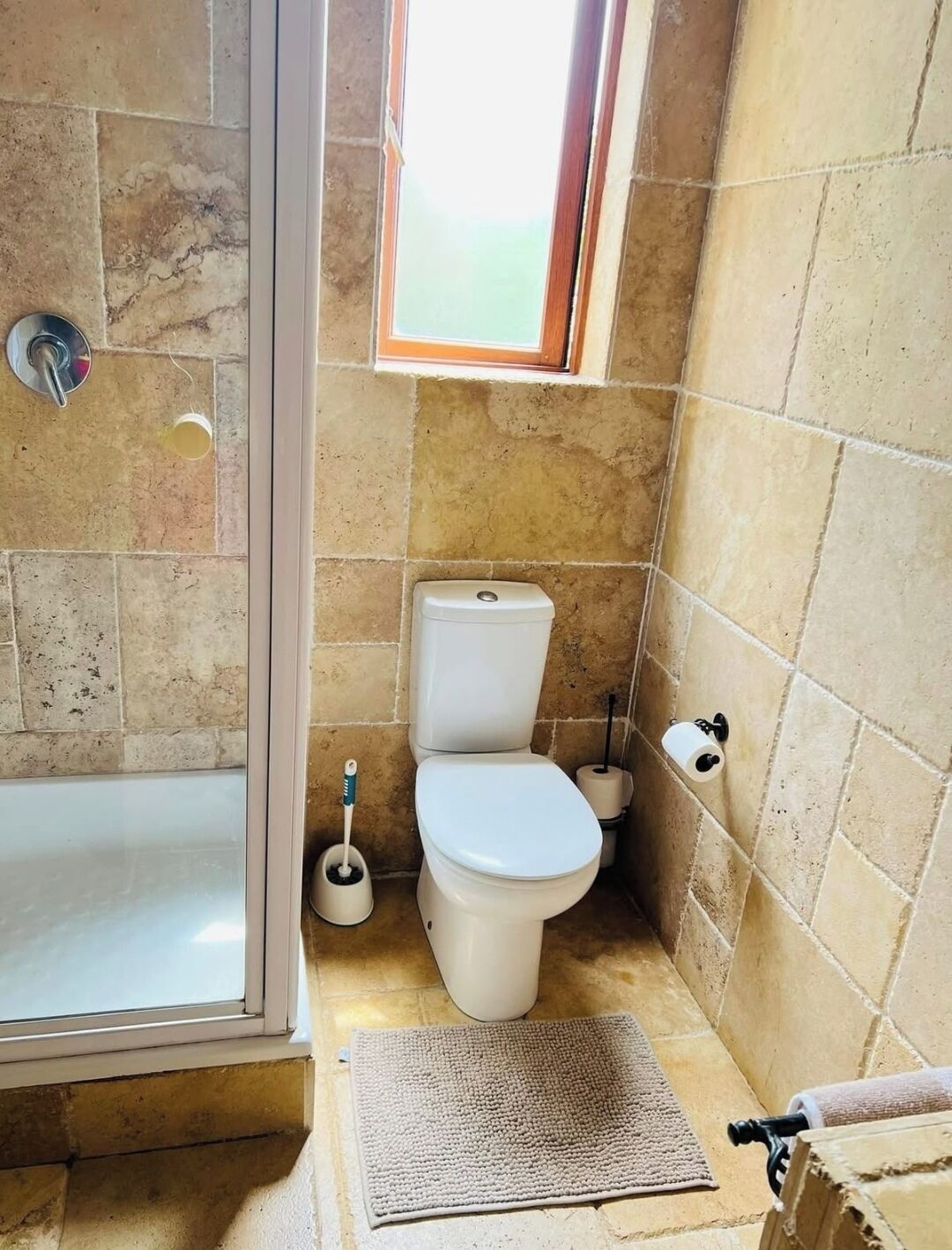 A bathroom with a shower, toilet, and a small window.