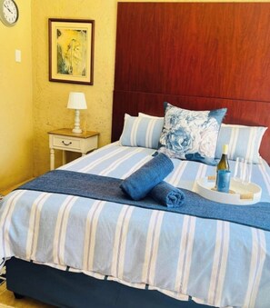 A bed with striped bedding, a wooden headboard, a nightstand with a lamp, and a framed picture on the wall.