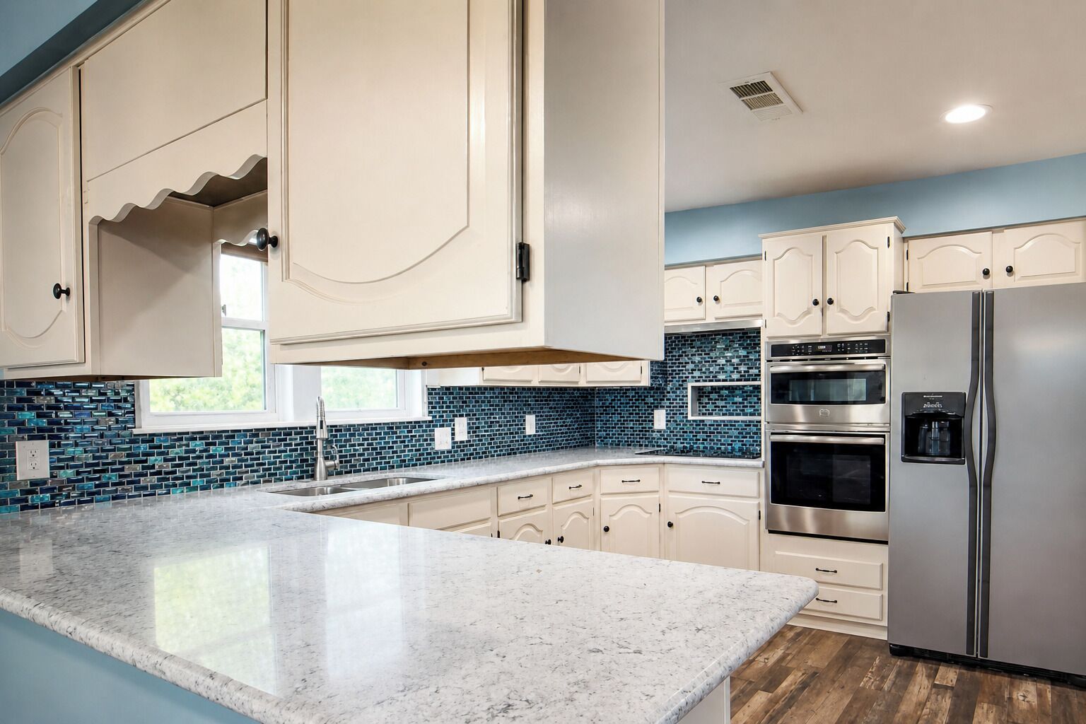 Eine Küche mit weißen Schränken, einer Arbeitsplatte aus Granit, einem Edelstahlkühlschrank und einer Rückwand mit blauen Fliesen.