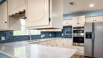 A kitchen with white cabinets, a granite countertop, a stainless steel refrigerator, and a blue-tiled backsplash.