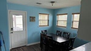 Uma área de refeições com mesa e cadeiras, uma porta com janela e um candeeiro no teto.