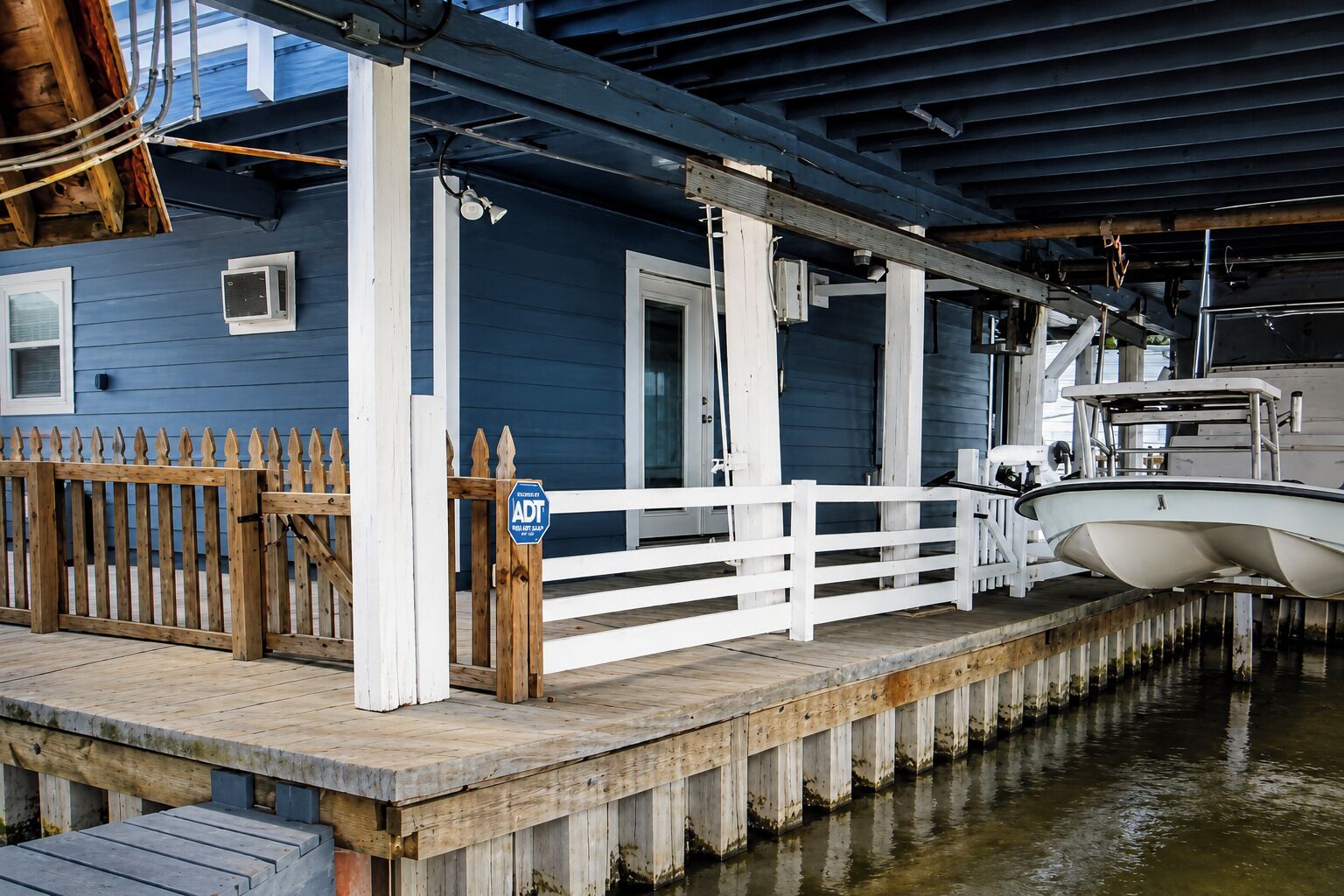 Un quai avec un bateau, une clôture en bois et un bâtiment à la façade bleue.