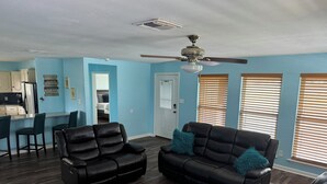 Uma sala de estar com um sofá e uma poltrona de couro preto, e um ventilador de teto.