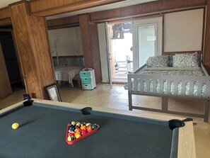 Ein Billardtisch mit Kugeln, ein Bett mit floralem Überwurf, ein Nachttisch mit Lampe und Blick ins Freie.