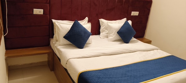A bed with white bedding and blue pillows, a wooden headboard, and a blue quilted blanket.