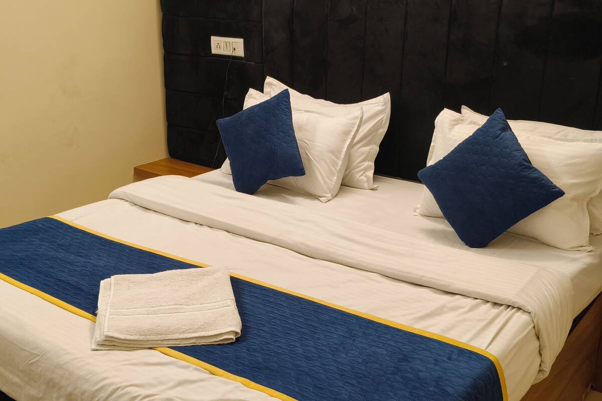 Ein ordentlich bezogenes Bett mit weißer und blauer Bettwäsche, ein gefaltetes weißes Handtuch und ein Nachttisch aus Holz.