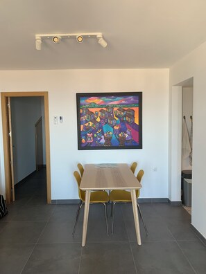 Un espace repas comprenant une table et des chaises, un luminaire au plafond, un tableau encadré et une porte donnant sur une autre pièce.