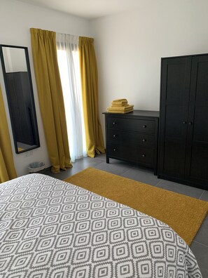 Une chambre à coucher avec un lit, une commode, une armoire, un miroir et des rideaux.