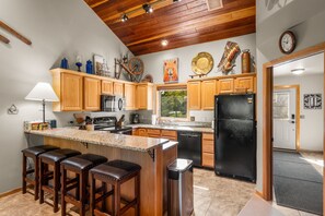 A kitchen with wooden cabinets, a granite countertop, a black refrigerator, and a window with a view of greenery. - 3BR Ski-In/Out Condo, Nordic Trails, Free Shuttle Access – Big Sky, MT (Big Sky)
