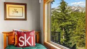 A bed with a green blanket, a pillow with 'SKI' text, a framed picture on the wall, and a window with a mountain view. - 3BR Ski-In/Out Condo, Nordic Trails, Free Shuttle Access – Big Sky, MT (Big Sky)