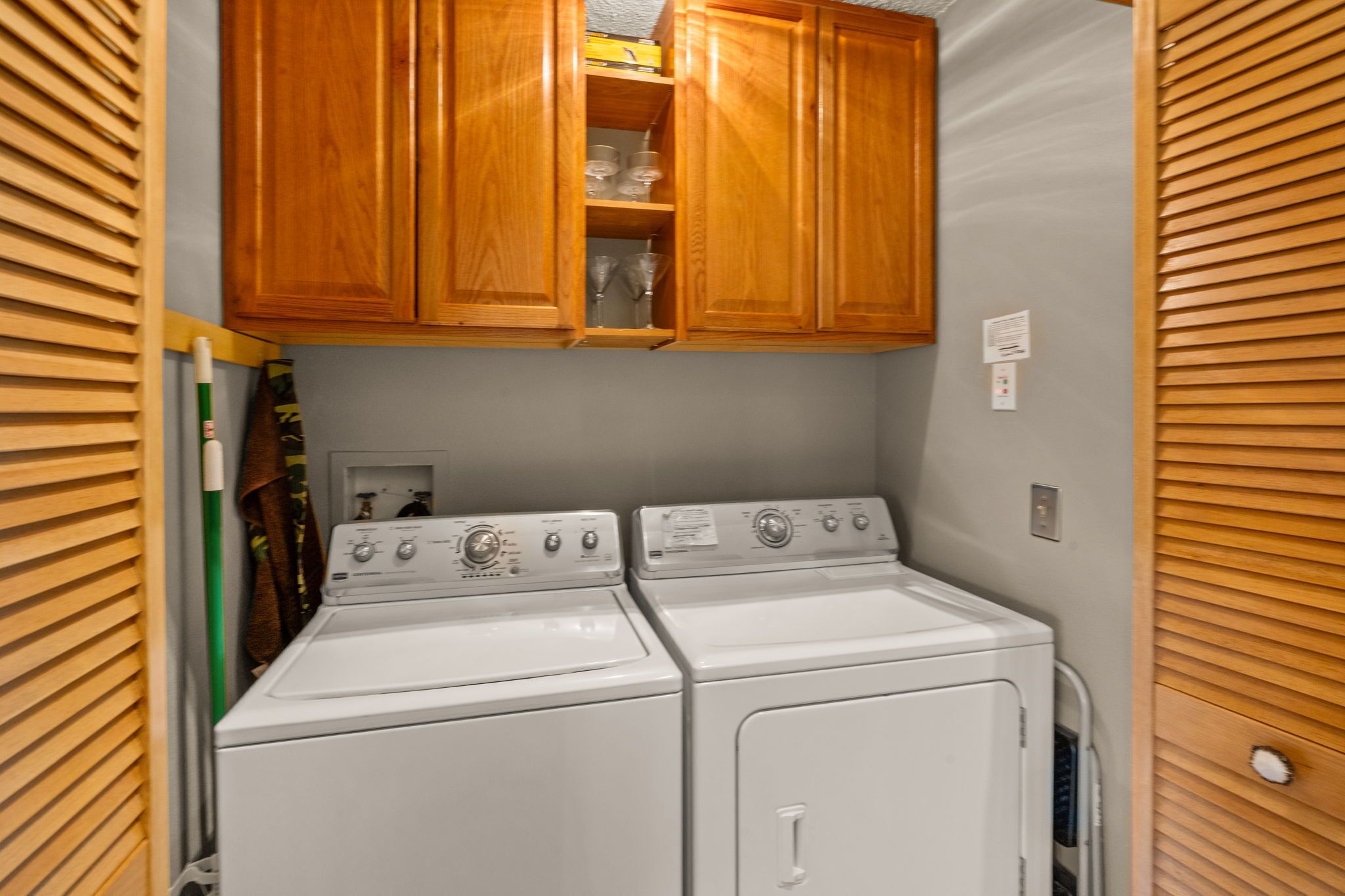 A laundry area with two stacked washers and dryers, wooden cabinets above, and a towel rack to the left.