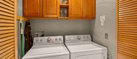 A laundry area with two stacked washers and dryers, wooden cabinets above, and a towel rack to the left.