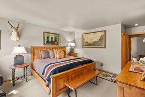 A bedroom with a wooden bed, a bench, a lamp, a small table, and two paintings on the wall. - 3BR Ski-In/Out Condo, Nordic Trails, Free Shuttle Access – Big Sky, MT (Big Sky)
