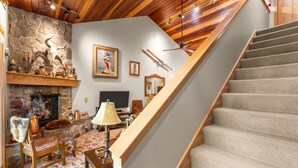 A cozy living room with a stone fireplace, a wooden staircase, and a television. - 3BR Ski-In/Out Condo, Nordic Trails, Free Shuttle Access – Big Sky, MT (Big Sky)