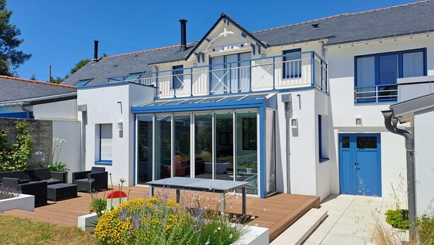 A modern house with a glass conservatory, outdoor seating, and a blue door.