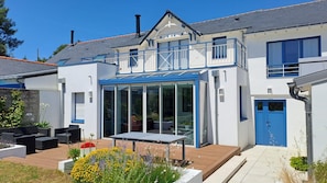A modern house with a glass conservatory, outdoor seating, and a blue door.