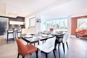 A modern kitchen with white cabinets, a dining area with a large table set for six, and a view of the outdoors through large windows.