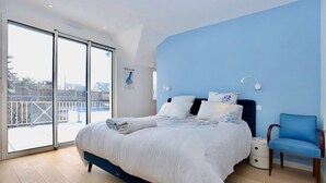 A bedroom with a bed, a chair, a nightstand, and a large window.