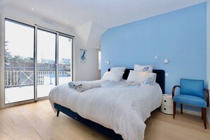 A bedroom with a bed, a chair, a nightstand, and a large window.