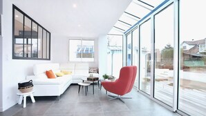 A modern living room with a white sofa, a red chair, a small table, and large glass windows.