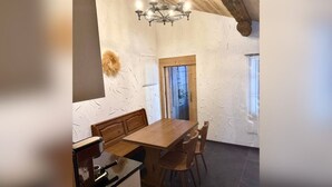A dining area with a wooden table and chairs, a chandelier, and a rustic ceiling.