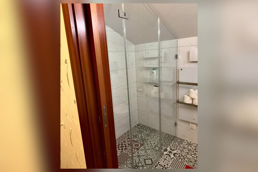 Ein Badezimmer mit Dusche, gefliesten Wänden und einem gemusterten Boden.
