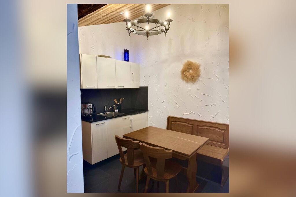 Une cuisine moderne avec des meubles blancs, une table à manger en bois et un lustre.