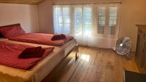 A bedroom with two beds, a fan, and a window with blinds.