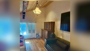 A living room with a wooden floor, a sofa, a table with chairs, a cabinet, and a fan.