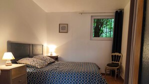 A bedroom with a bed, bedside table, lamp, chair, and a window with a view of trees.