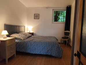 Une chambre à coucher comprenant un lit, une table de chevet, une lampe, une chaise et une fenêtre donnant sur des arbres.
