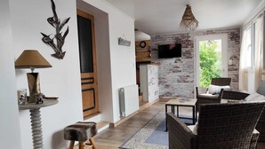 A living room with a TV, wicker furniture, a small stool, and a decorative wall piece.