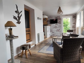 Un salon avec un téléviseur, des meubles en osier, un petit tabouret et un élément décoratif mural.