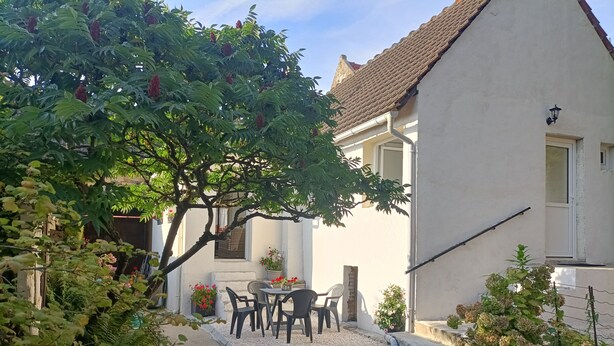 A courtyard with a table and chairs, surrounded by plants and a building with a tiled roof.