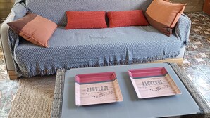 A wooden wall with a painting of sailboats, a patterned sofa with red cushions, and a wicker coffee table with two trays.