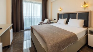 Una habitación de hotel con una cama grande, un escritorio, una silla, una mesita de noche y un ventanal con cortinas.