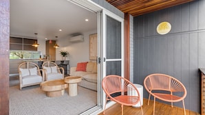 A modern living area with wicker furniture, a wooden ceiling, and a glass door leading to an outdoor space. - Relaxed 2 Bed Coastal Stay Near the Lake (Buff Point)