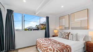 A bedroom with a large bed, a window with curtains, a bedside table with a lamp, and a wall-mounted artwork. - Relaxed 2 Bed Coastal Stay Near the Lake (Buff Point)