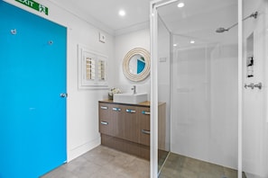 Um banheiro com porta azul, pia, espelho e chuveiro.