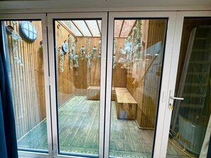 A room with a sliding glass door leading to an outdoor area with a wooden deck and a bench. - Spacious apartment with private patio (Greater London)