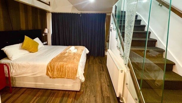 Ein Hotelzimmer mit einem Bett, einem roten Sessel, einer Glasstufenkonstruktion und einem dunklen Vorhang.
