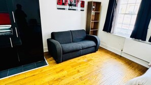 Ein Wohnzimmer mit einer schwarzen Couch, einem Holzschrank, einem Gemälde an der Wand und einem Fenster mit Vorhängen.