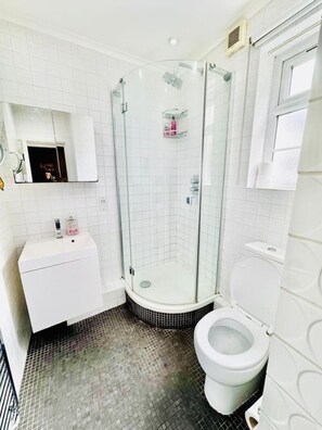 A bathroom with a glass-enclosed shower, a white sink, and a toilet. - Cosy one bedroom flat near Aldgate East station (Greater London)