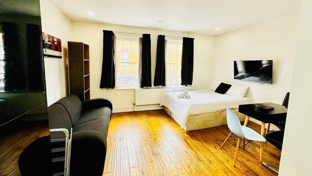 Ein kleines Zimmer mit Bett, Schreibtisch, Sessel, Sofa und Fernseher.