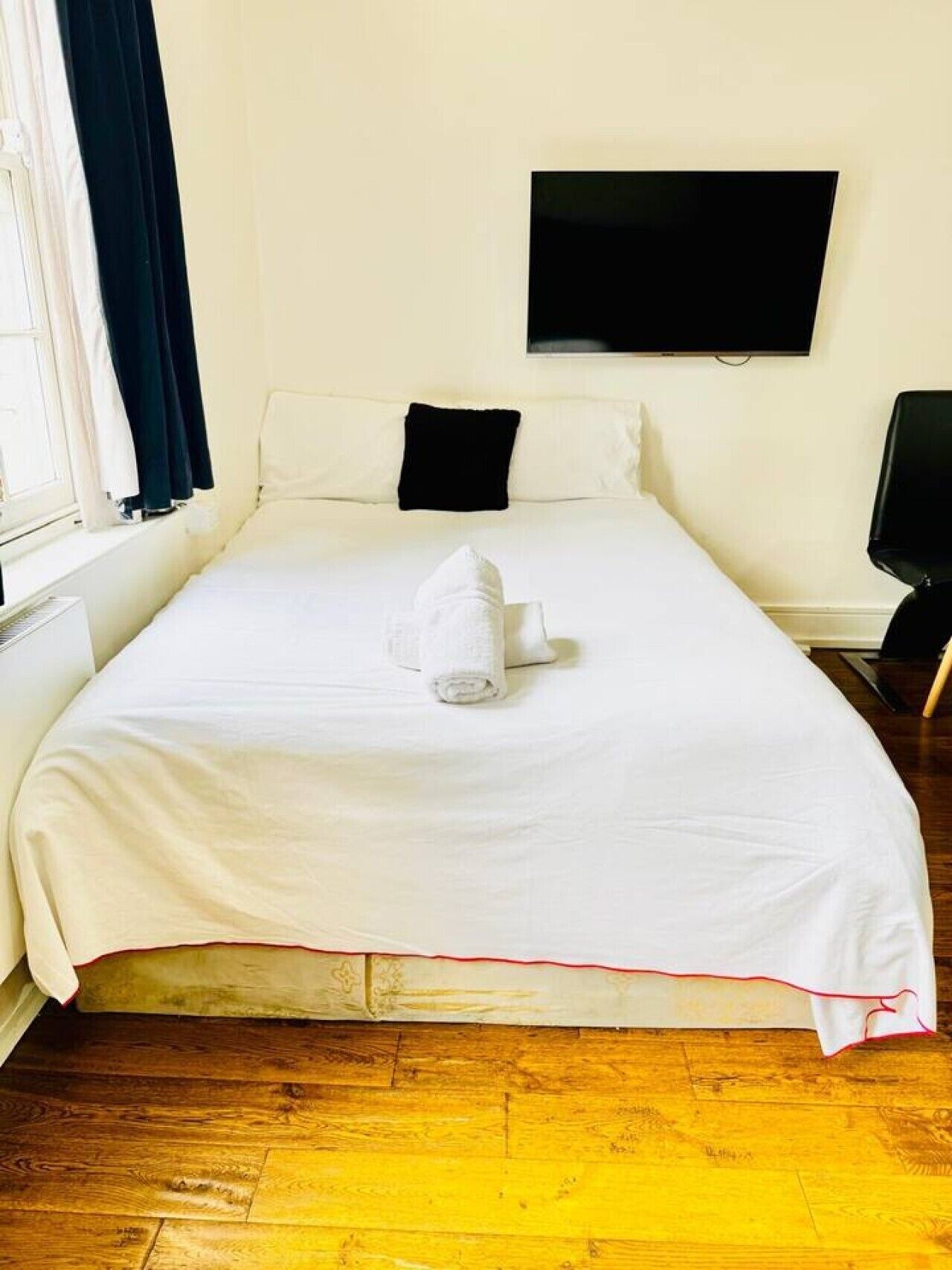 Ein Hotelzimmer mit Bett, flachbildfernseher an der Wand und einem Fenster mit Vorhängen.
